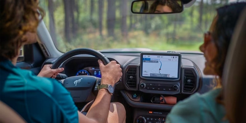 two people driving through the woods smiling inside the car