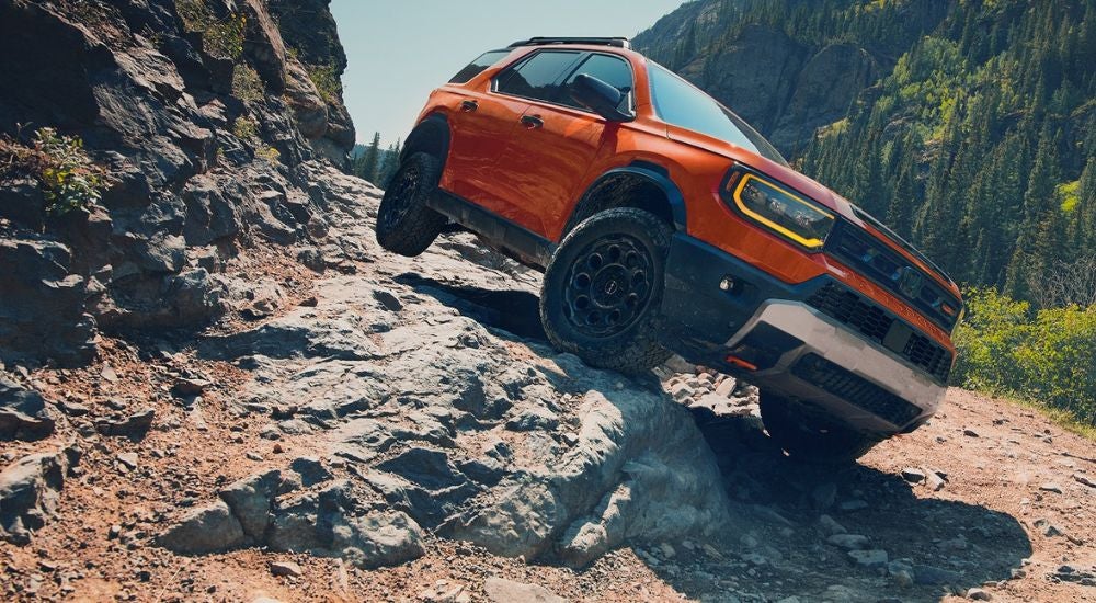 An orange 2027 Honda Passport TrailSport climbing down rocky terrain.