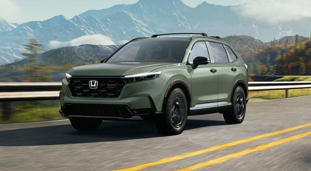 A green 2027 CR-V TrailSport Hybrid driving past a guard rail.