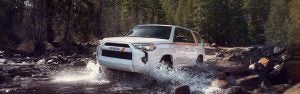 A white, Toyota 4Runner drives through a stream.