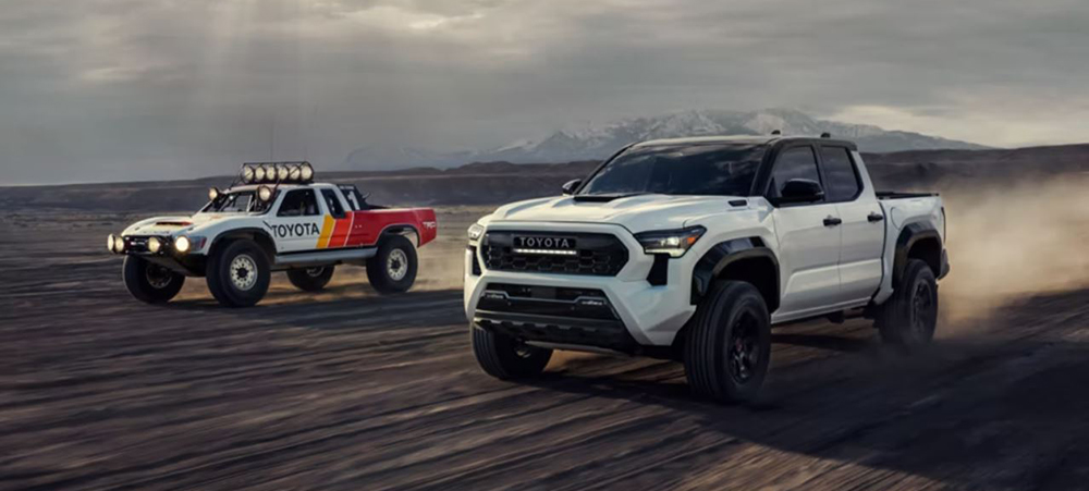Two Toyota Tacomas drive through a desert, kicking up dirt.