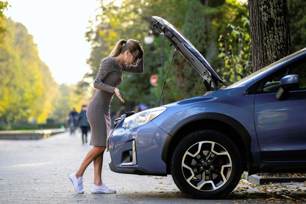 Woman looking under the hood of her blue car