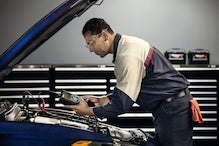 Man leaning over the open hood of a car while checking its engine