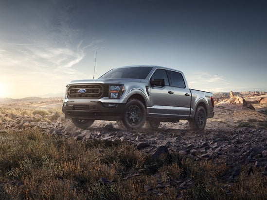 A grey ford truck travelling over rocks during sunset 