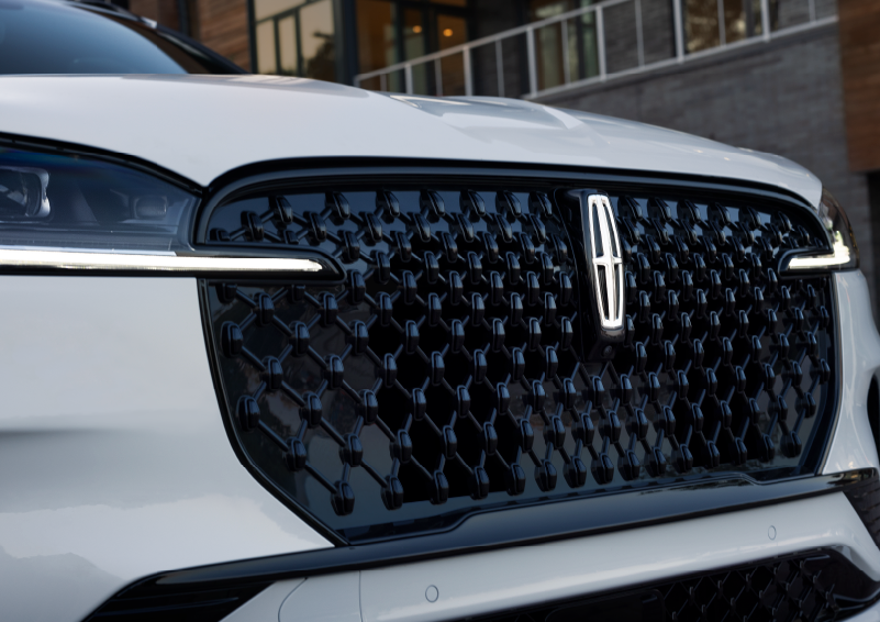 A close-up view of the emblem on a white 2025 Lincoln Aviator, prominently displayed over a sleek black grille.