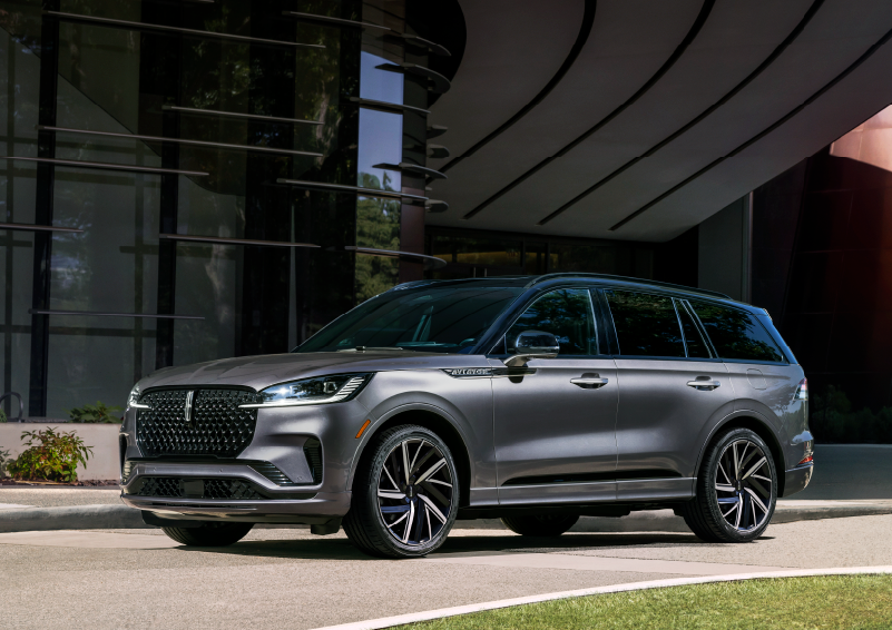 2025 silver Lincoln Aviator parked on a driveway under a sunny sky, outside a modern building with large windows and an elevated walkway, near London, KY