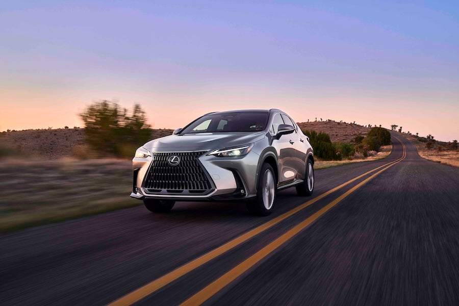 A gray 2025 Lexus NX SUV driving down a road at sunset