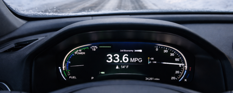 Car dashboard displaying fuel economy while driving on a snow-covered road during winter conditions.