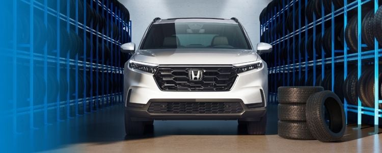 Authorized Tire Center image featuring a white Honda SUV centered between blue-lit tire racks with stacked tires in an indoor service facility.