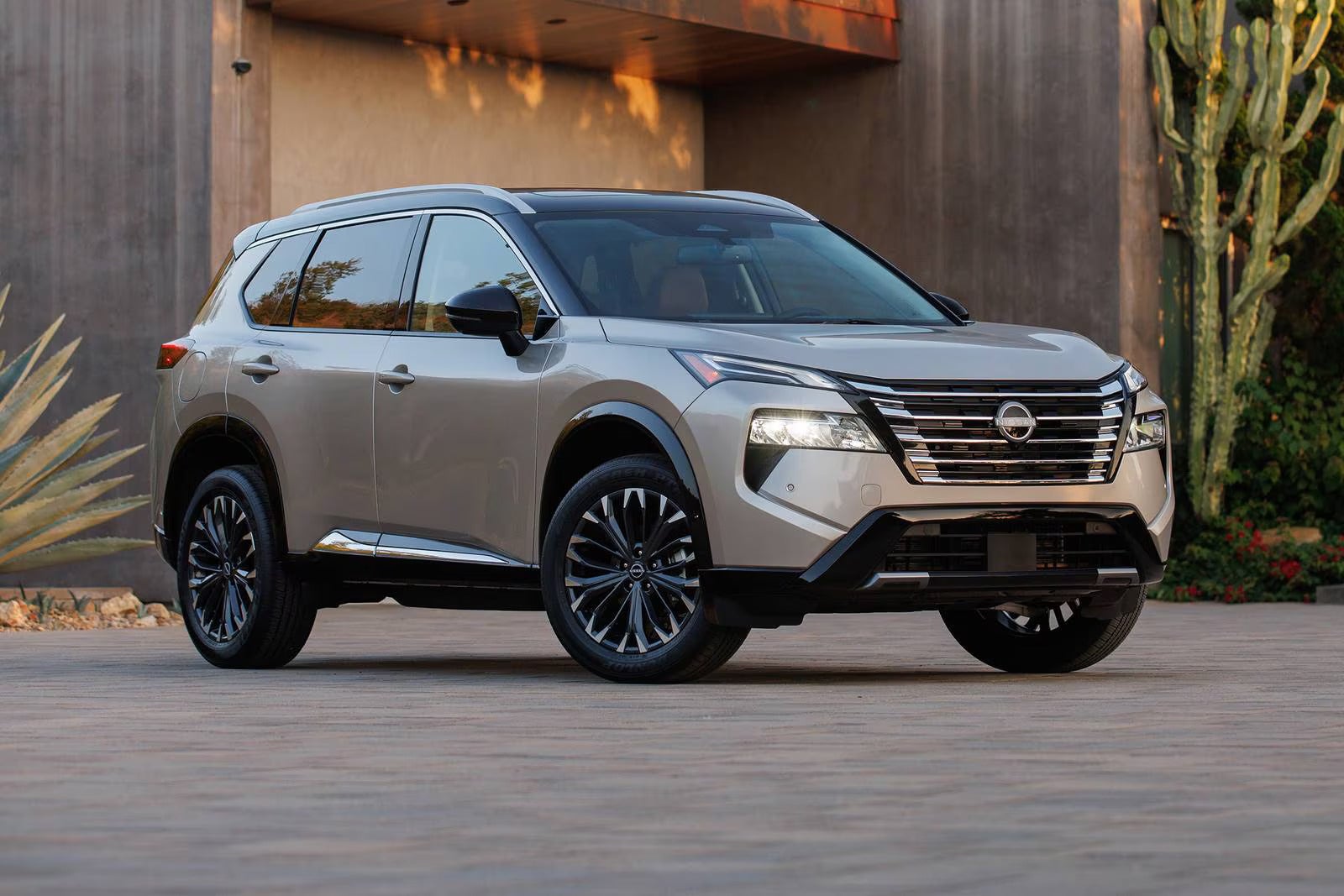 2025 Nissan Rogue Platinum in a sleek Champagne Silver finish parked in front of a modern home with stylish accents.