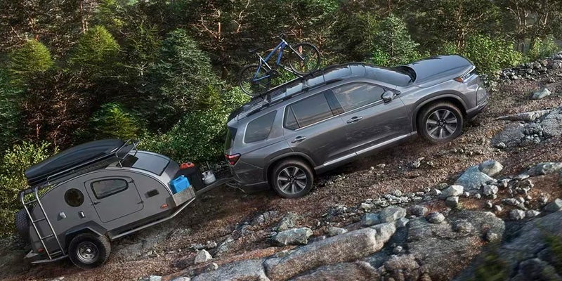 A photo of a 2024 Honda pilot towing a camper up a hill