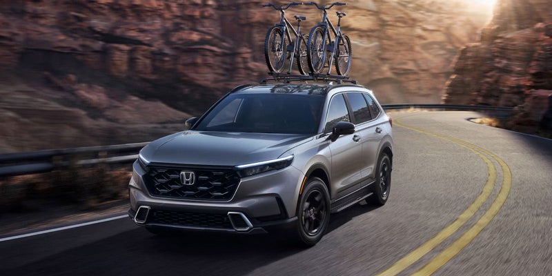 A grey 2025 Honda CR-V with a bike rack on top driving down a mountain road