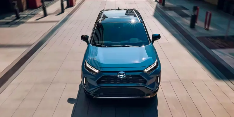 A blue Toyota RAV4 Hybrid driving down the road near Woodrum Toyota of Macomb.