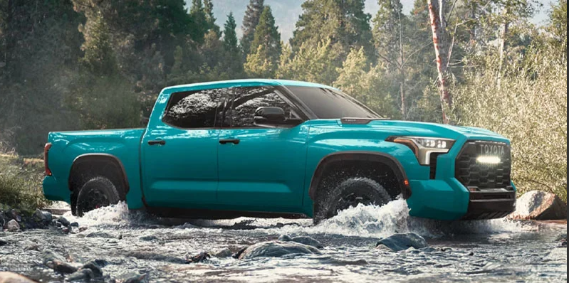A blue 2026 Toyota Tundra off-roading through a stream of water.