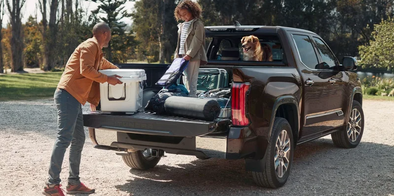 A man loading a cooler in to the back of a 2025 Toyota Tundra while his daughter is standing in the back.