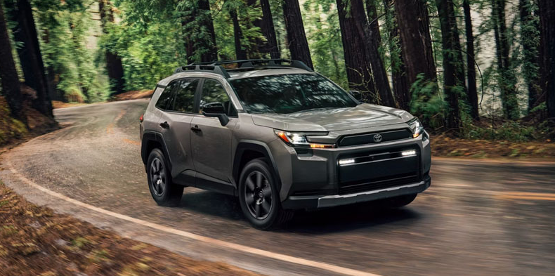 A green 2026 Toyota RAV4 driving down a forest road.