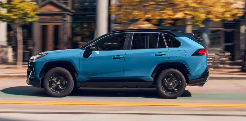 A blue 2024 Toyota RAV4 Hybrid driving down the street.