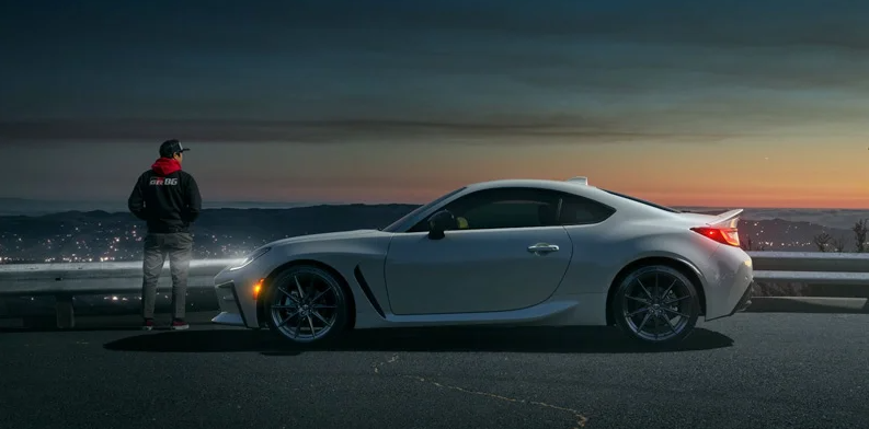 A man standing next to a silver 2024 Toyota Gr8g with the sunset in the backround.