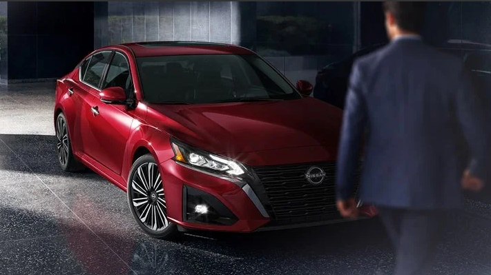 A man walking around the front of a red 2024 Nissan Altima.