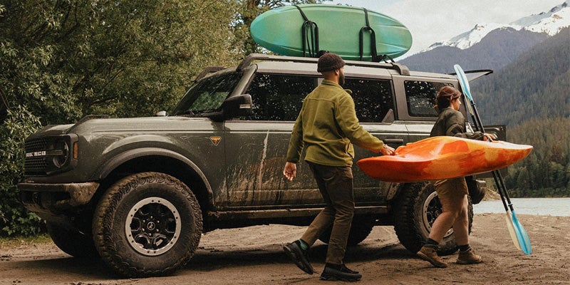Ford Bronco parked by a lakeside with kayaks mounted on roof and outdoor gear