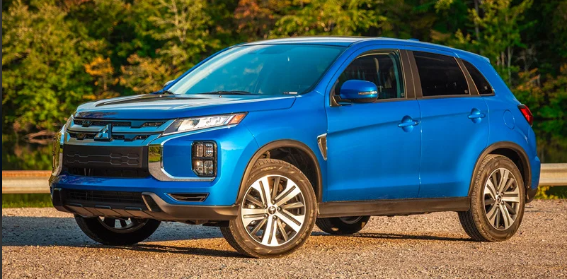 A blue Mitsubishi Outlander Sport parked on a gravel road with trees in the background.