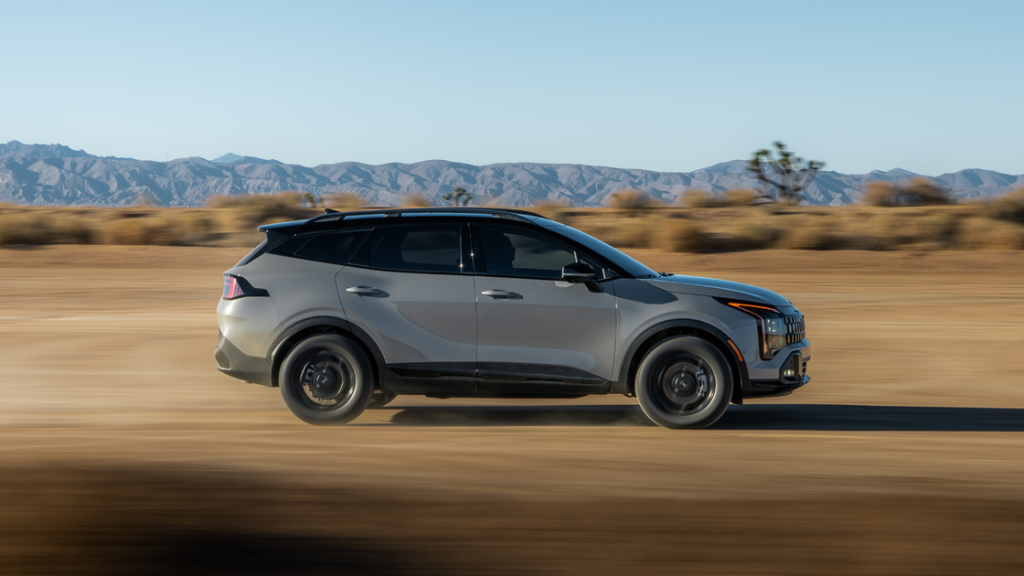 2026 Kia Sportage HEV hybrid SUV driving off-road in desert, side profile, gray exterior.