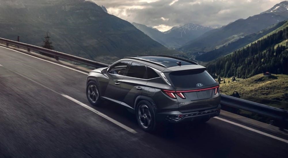 A grey 2023 Hyundai Tucson is shown driving past mountains on a cloudy day.