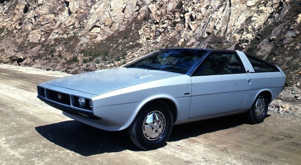 A grey 1974 Hyundai Pony Coupe angled left while parked on a dirt road.