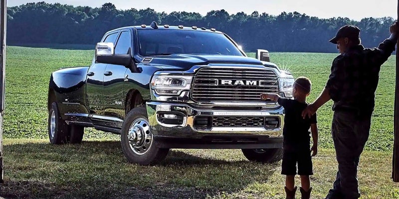 A man and a boy stand beside a black Ram truck in a grassy field with trees in the background.