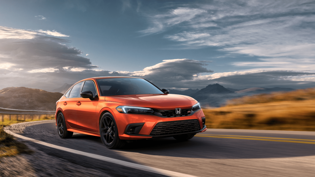 A vibrant orange 2024 Honda Civic Si Sedan driving on a scenic mountain road under a dramatic cloudy sky.