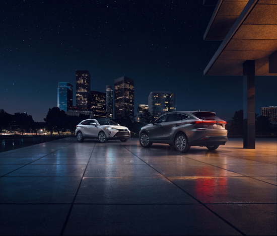 Two sleek cars are parked on a glossy, tiled surface at night, with a city skyline in the background. The scene conveys a modern, urban elegance.