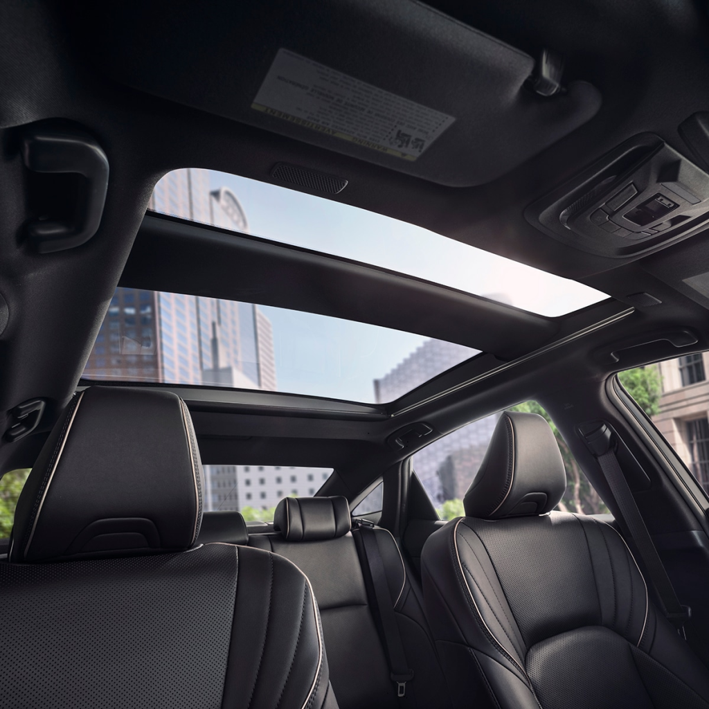 View from inside a car showcasing a sunroof against a city skyline. Sleek black leather seats convey luxury and modernity. Bright daylight outside.
