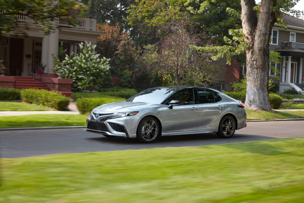 Silver sedan driving along a suburban street lined with lush greenery and historic homes. The scene feels calm and picturesque, capturing a serene drive.