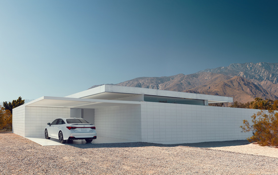 Modern white house with clean lines and a flat roof, set against a mountain backdrop. A white car is parked in the driveway, under a clear blue sky.