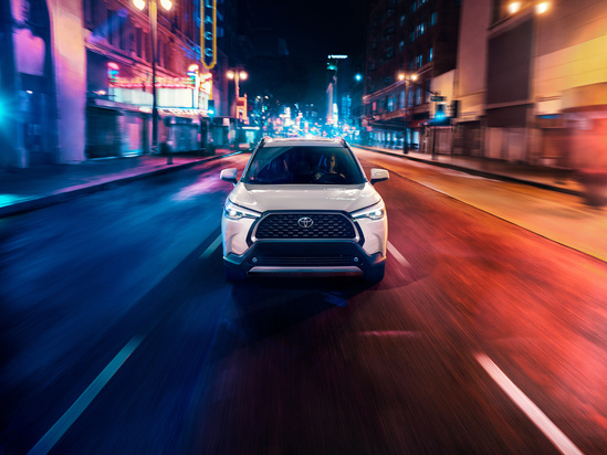 White SUV driving at night on a vibrant city street, illuminated by blue and red neon lights, creating a dynamic and futuristic atmosphere.