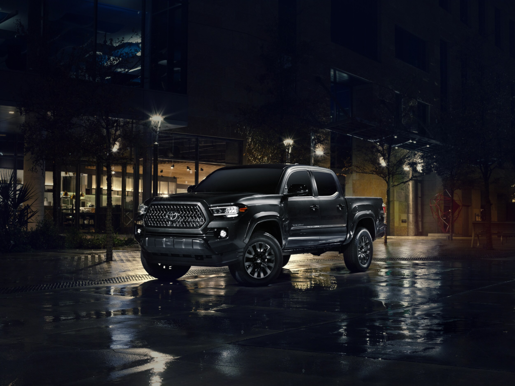 Sleek black pickup truck parked on wet pavement in an urban setting at night. Warm streetlights reflect on the sidewalk, creating a sophisticated, serene mood.