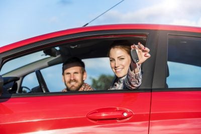 People in a red car, with a woman in the driver seat holding a key fob out of the window