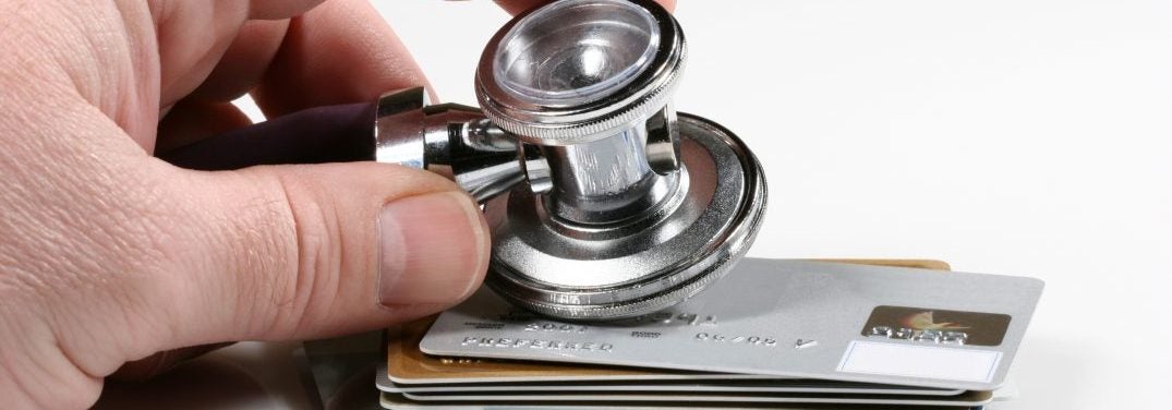 Person holding a stethoscope on a pile of credit cards