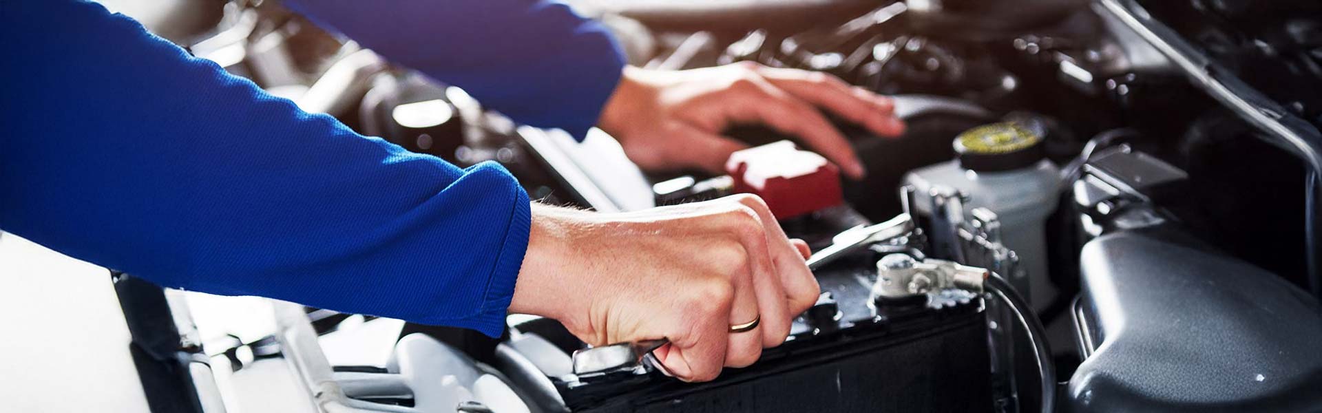 Hands in blue long-sleeved shirt using a wrench to repair a car battery in an open engine.