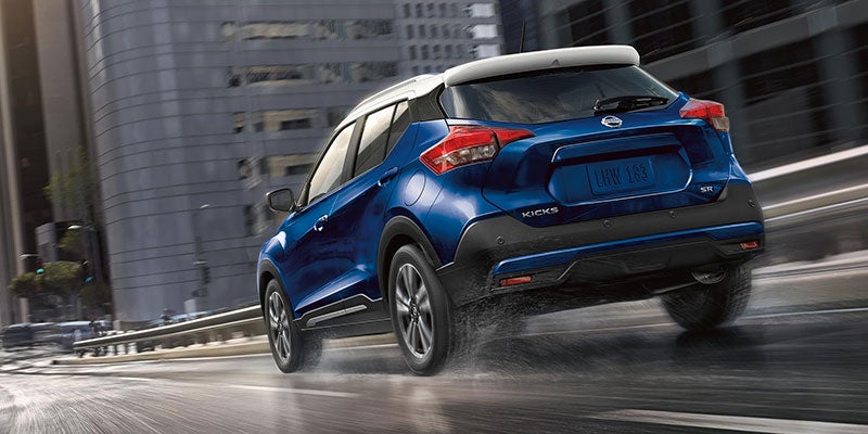 Nissan Kicks driving on a wet road, with buildings blurred in the background.