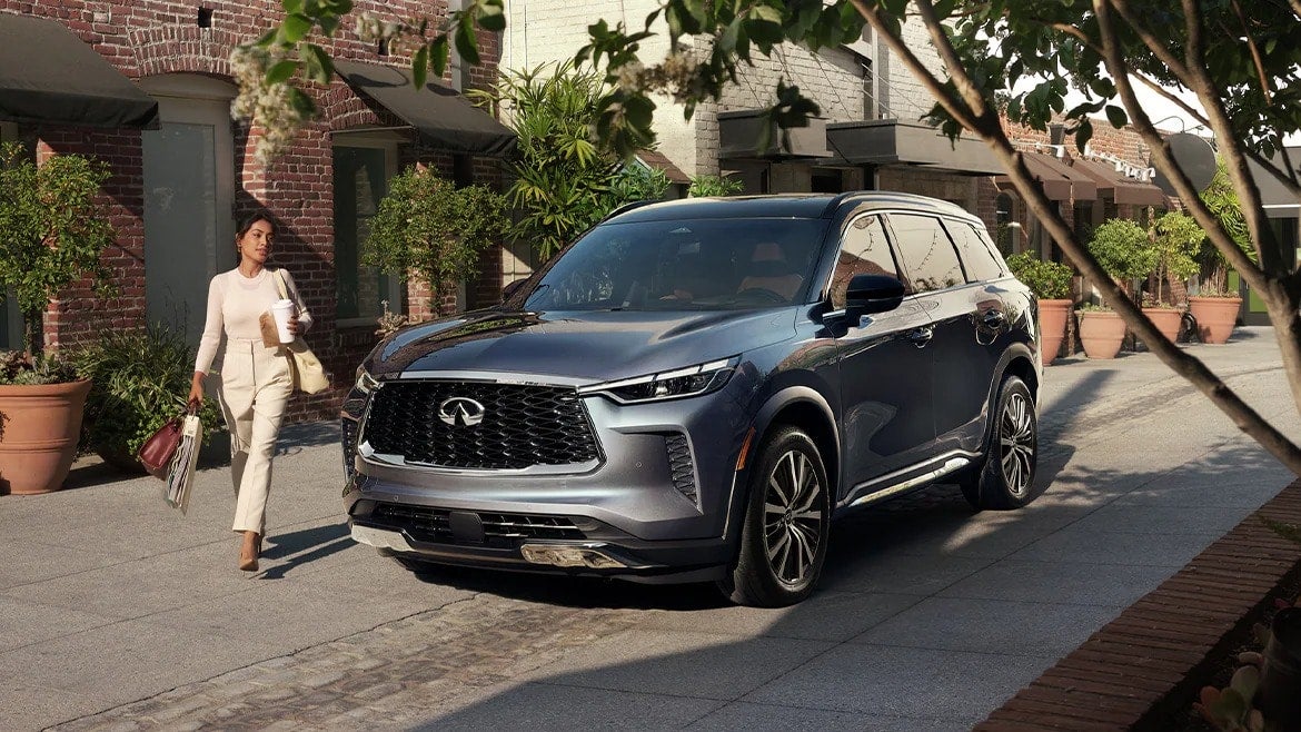 A woman walking next to a gray 2023 INFINITI QX60