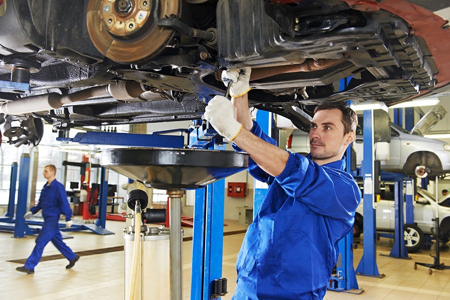 Technician working under a lifted car in a service bay.