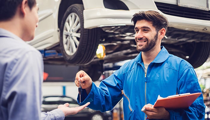Auto technician handing keys to a customer in a car service garage.