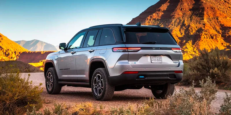 A silver 2025 Jeep Grand Cherokee parked in a sandy area near 