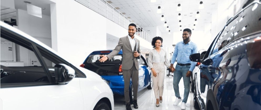 Car dealership showroom with salesperson assisting customers among vehicles.