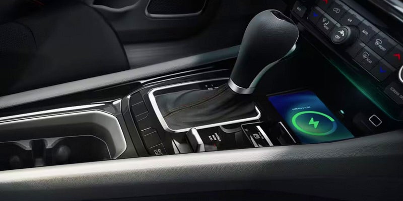 A smartphone charging wirelessly in a car's center console next to the gear shift.