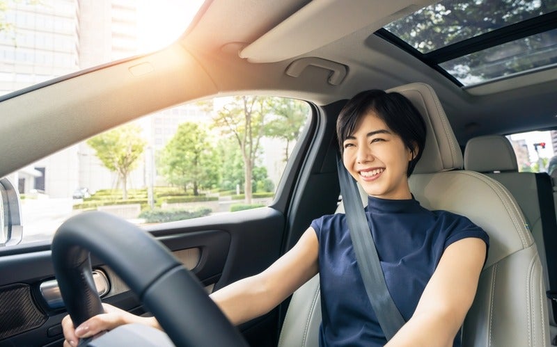Attractive young woman with short dark hair, wearing a blue shirt, smiling and safely buckled into a car.