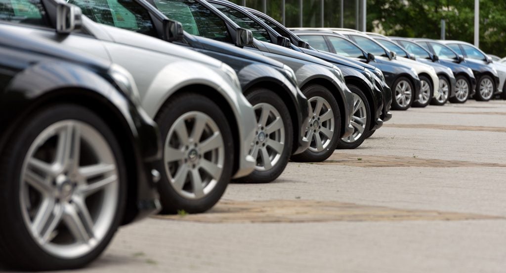 A line of new black and grey cars parked outdoors, showing their front wheels and partial sides.