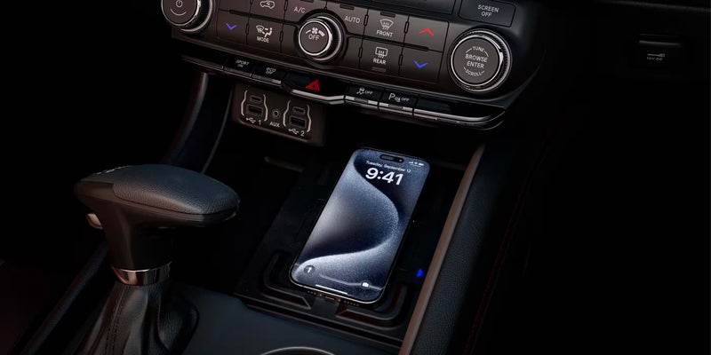 An iPhone charges wirelessly in a car's center console tray, with climate controls and USB ports visible above.