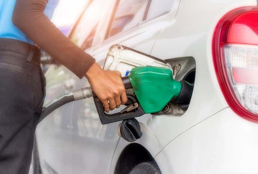 A person's hand inserts a green gas nozzle into a white car's gas tank.